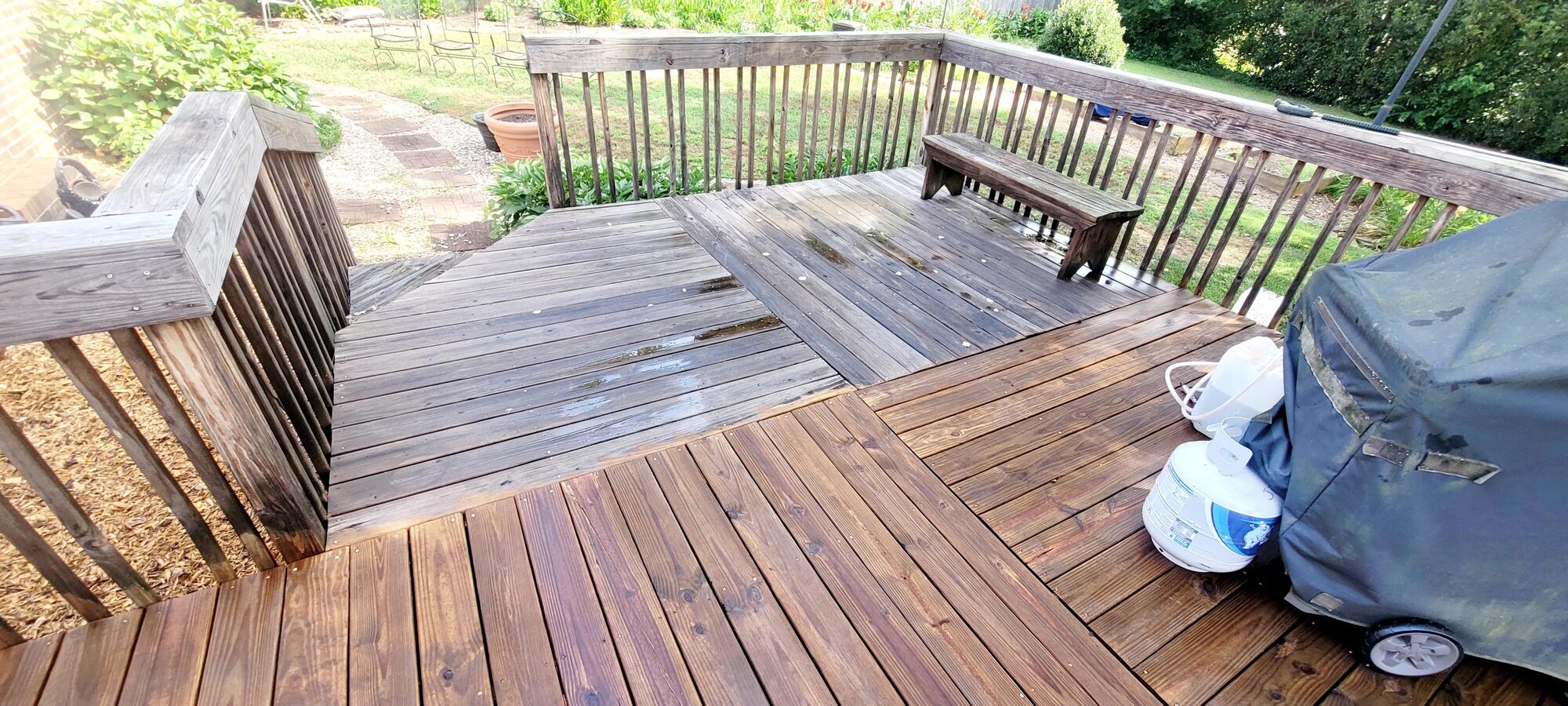 A deck halfway through staining, weathered gray on one side and freshly stained reddish brown on the other