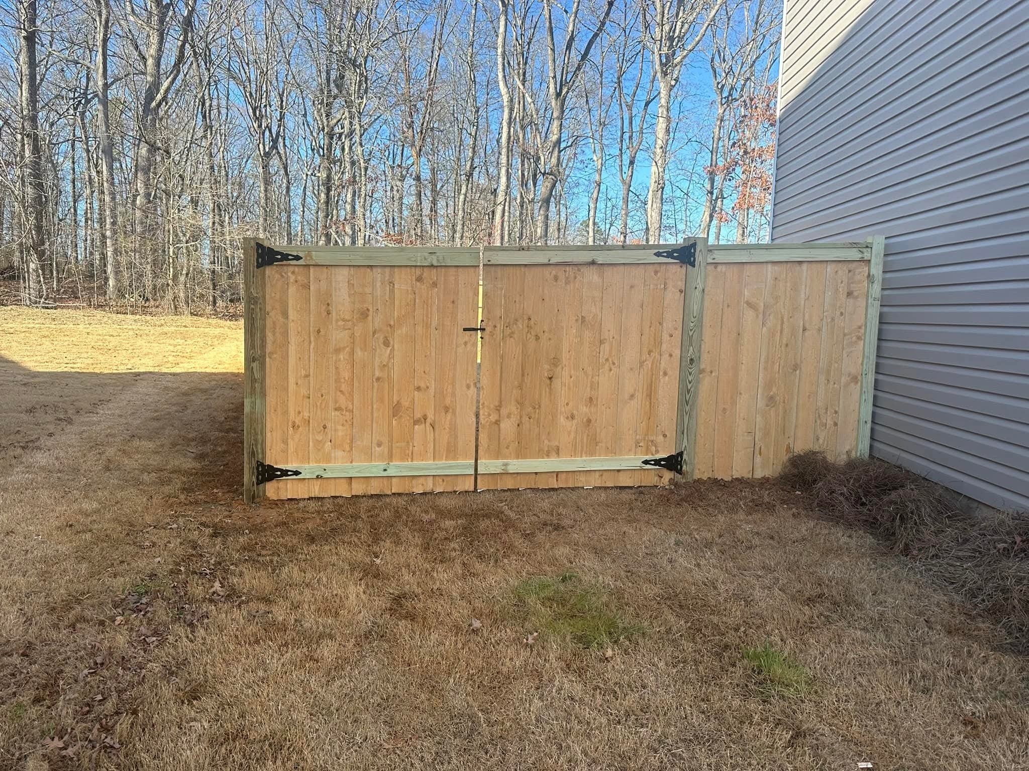 A newly built wood double gate and fence, unstained, in front of a home with gray siding